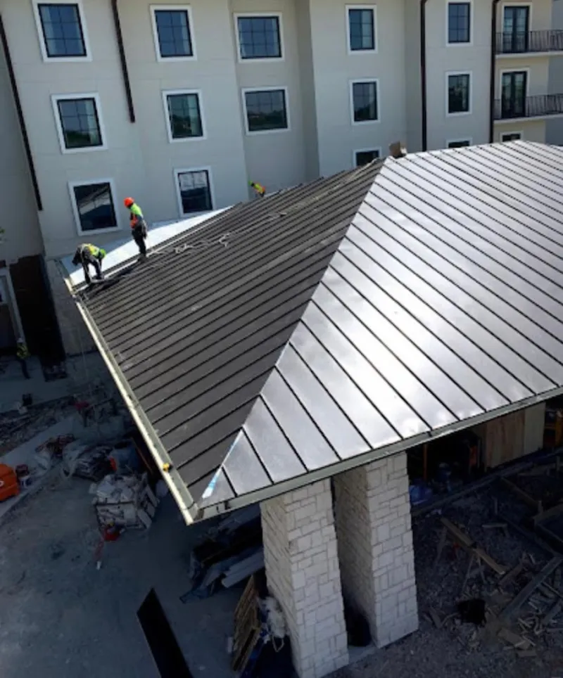 Crew installing standing seam metal roof panels on a commercial project in Troy